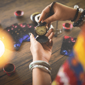 Manos de una tarotista profesional sosteniendo un reloj antiguo sobre una mesa con cartas para analizar las líneas temporales